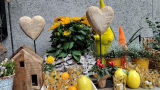 Dekoratives Arrangement mit gelben Blumen, Zitronen, Kerzenhaltern, Holzherzen und kleinen Pflanzen auf einem Regal.