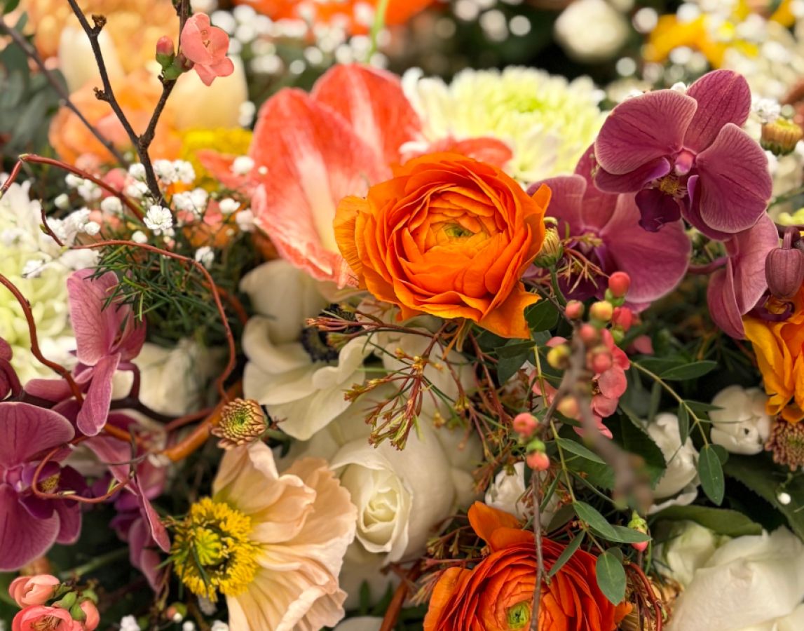 Außenansicht eines Blumenladens mit Schaufenster voller Pflanzen, Blüten, Dekorationen und einer großen geflochtenen Figur.