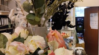 Dekoratives Arrangement mit roséfarbenen Rosen und Zweigen in Vasen, präsentiert im Innenraum eines Büros.